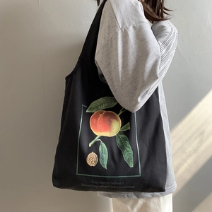 Détail du sac cabas en toile noire avec imprimé pêche porté par un mannequin femme