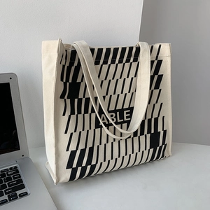 Close-up of cream canvas tote bag featuring ABLE text and geometric stripe pattern