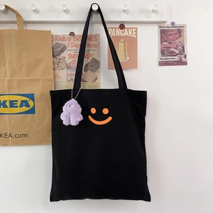 Close-up of black canvas tote bag with orange smiley face and purple plush monster charm
