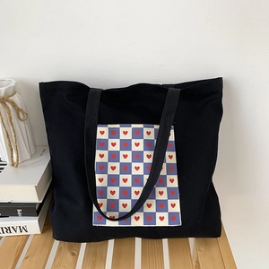 Close-up of black canvas tote bag with heart checkerboard patch on a wooden table