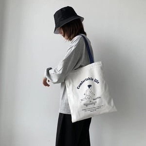 Detailed side view of white canvas tote bag with blue straps on a model's shoulder
