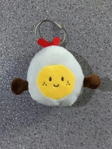 Close-up of plush poached egg keychain with smiling embroidery and red heart detail