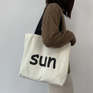 Canvas tote bag with 'sun' print and black straps shown on shoulder of model