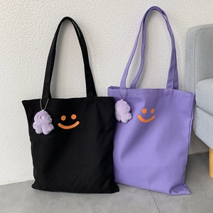 Detail of canvas tote bag with orange smiley face and purple cloud plush charm