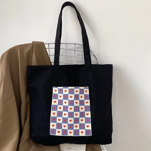 Detail of black canvas tote bag featuring a checkered heart pocket on a white chair