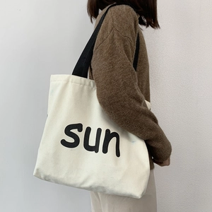 Detail of white canvas tote bag with sun lettering and black strap worn over a sweater