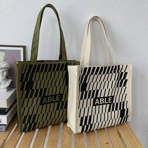 Detail of large canvas tote bag with geometric stripes and bold ABLE text on wooden stool