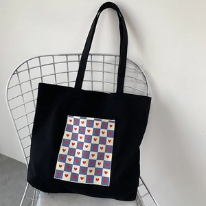 Detail of black canvas tote bag featuring a blue checkered pocket with red heart patterns