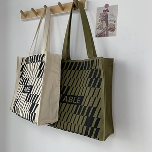 Detail of large canvas tote bags with ABLE print and stripes hanging on wooden hooks