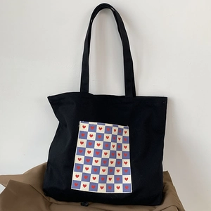 Detail of a black canvas tote bag featuring a checkered pocket with red heart patterns