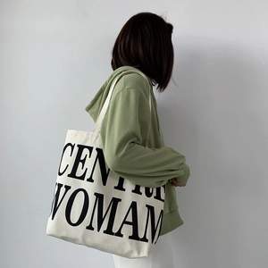 Detailed view of heavy canvas tote bag with GENTLEWOMAN text on a green hoodie model
