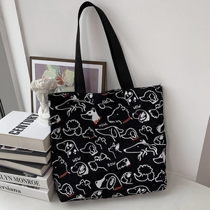 Detail of black canvas tote bag featuring white dog illustrations on a white surface