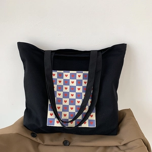 Detail of black canvas tote bag featuring a purple checkered heart patch and wide straps