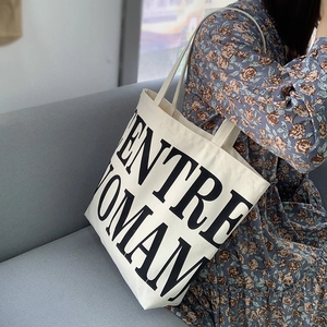 Close-up of a large beige canvas tote bag with black ENTRE WOMAN lettering print