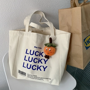 Canvas tote bag with Lucky print and orange persimmon plush charm on a white chair