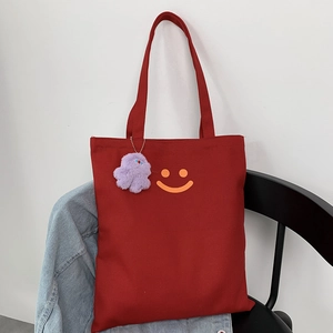 Detail of red canvas tote bag with yellow smiley face print and purple plush charm