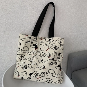 Detail of canvas tote bag showing dog illustrations and black nylon handles in a cozy setting