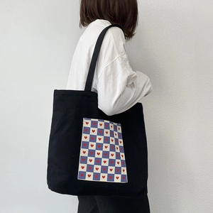 Close-up of black canvas tote with blue checkerboard pocket and red heart prints