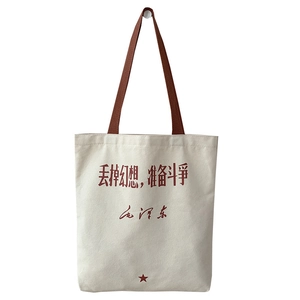 Minimalist canvas tote bag with red calligraphy print and brown handles on white wall