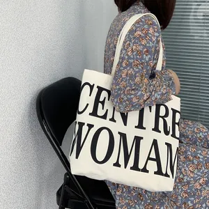 Detail of large canvas tote bag with black CENTRE WOMAN text on a female model