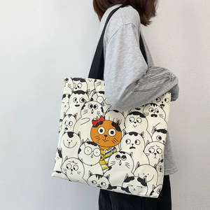 Detailed view of cream canvas tote bag with cute cartoon cat patterns and black straps