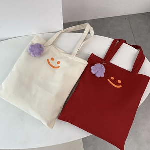 Detail of canvas tote bags with orange smiley prints and purple plush monster charms