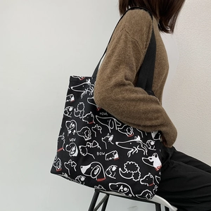 Detailed shoulder view of a black canvas tote bag with white dog illustrations and red accents
