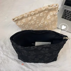Detail of floral jacquard cosmetic bags in beige and black with relief flower patterns