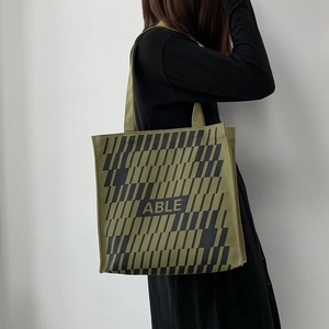 Detail showing olive green canvas tote bag with black geometric pattern and ABLE text