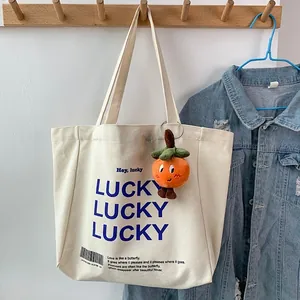 Detail of off-white canvas tote bag featuring blue LUCKY print and orange plush charm