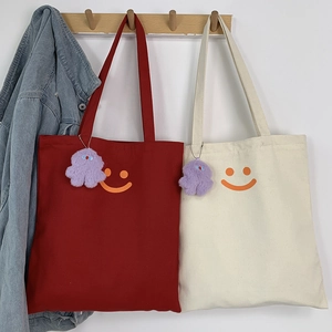 Detail of red and cream canvas tote bags with orange smiley face and purple plush charms
