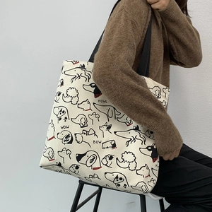Close-up of off-white canvas tote bag featuring artistic dog prints and black fabric straps