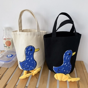 Detail of canvas bento bags with cute duck prints and 3D webbed feet on a wooden bench