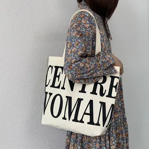 Close-up of white canvas tote bag with black CENTRE WOMAN text on floral dress model