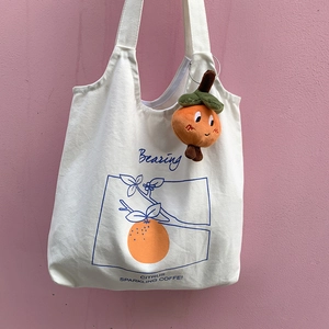 Detail of white canvas tote with citrus print and cute orange plush doll keychain