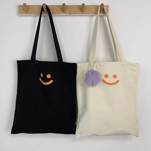Detail of canvas tote bags in black and cream featuring a minimalist orange smiley face