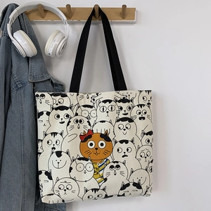 Detail of cream canvas tote bag with cartoon cat prints and orange cat accent