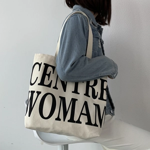 Model wearing a large canvas tote bag with bold black text print in a clean setting