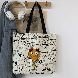 Detail of canvas tote bag featuring cute cartoon cat prints and sturdy black straps
