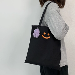 Detail of black canvas tote bag with orange smiley face and purple plush charm