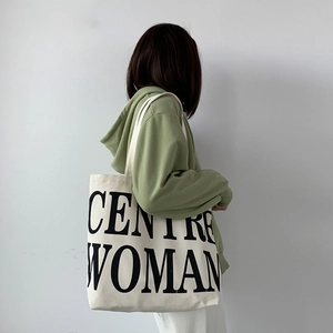 Detail of large canvas tote bag with black CENTRE WOMAN text on casual green hoodie