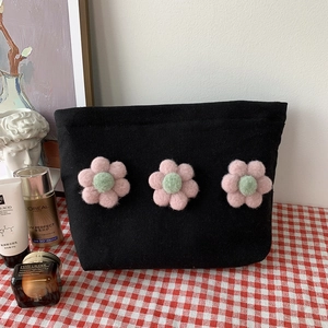 Detail of black canvas makeup bag featuring three 3D plush floral embellishments