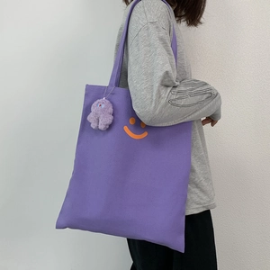 Close-up of purple canvas tote bag with orange smiley face and plush charm