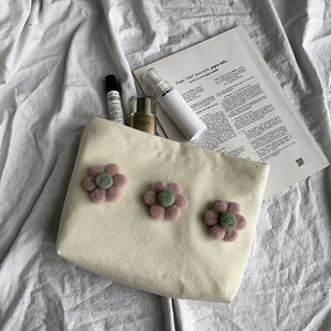 Detail of cream canvas makeup bag with 3D pink floral pom-poms and zipper closure