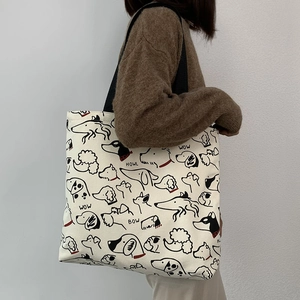 Close-up of cream canvas tote bag with cartoon dog prints and black woven strap