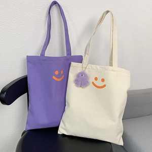 Detail of purple and beige canvas tote bags with orange smiley face and plush pendant