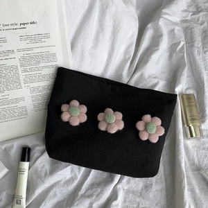 Close-up of black canvas cosmetic bag with three 3D plush flowers on white cotton fabric