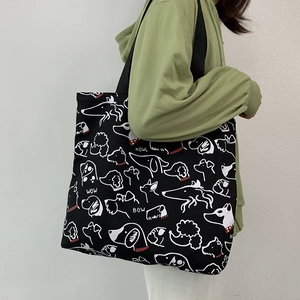 Close-up of canvas tote bag with black strap and white dog line art illustrations