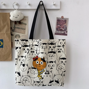 Detail of canvas tote bag featuring cute cartoon cats pattern on a white studio wall