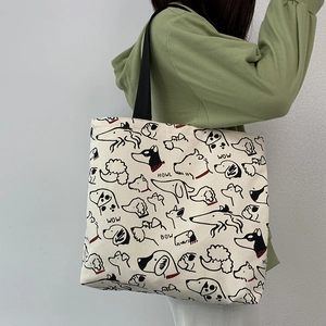 Detail view of canvas tote bag with cartoon dog prints and black woven shoulder straps
